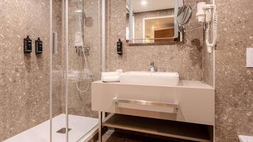 A modern bathroom with a glass-enclosed shower, a white sink with a mirror above it, and a hairdryer mounted on the wall.