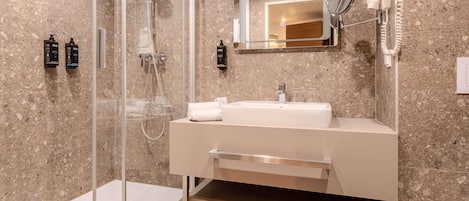 A modern bathroom with a glass-enclosed shower, a white sink with a mirror above it, and a hairdryer mounted on the wall.
