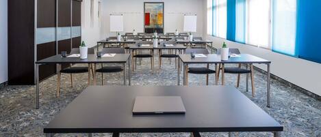 A conference room with tables, chairs, and a large window with blinds.
