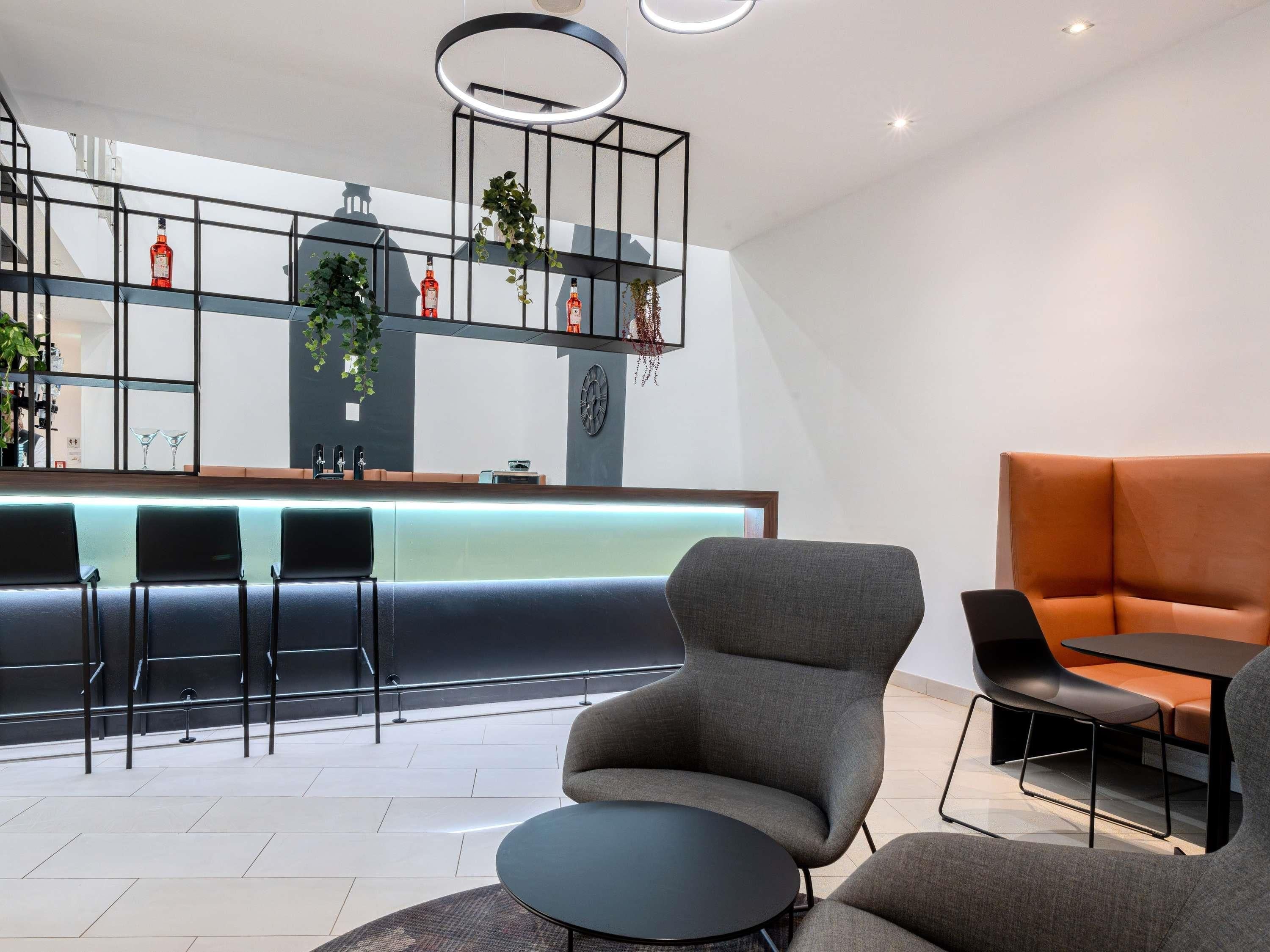 A modern lounge area with a bar, seating, and a decorative plant arrangement.