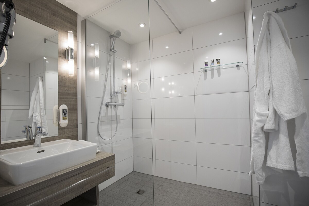 A modern bathroom with a large mirror, a sink, a shower, and a towel rack.
