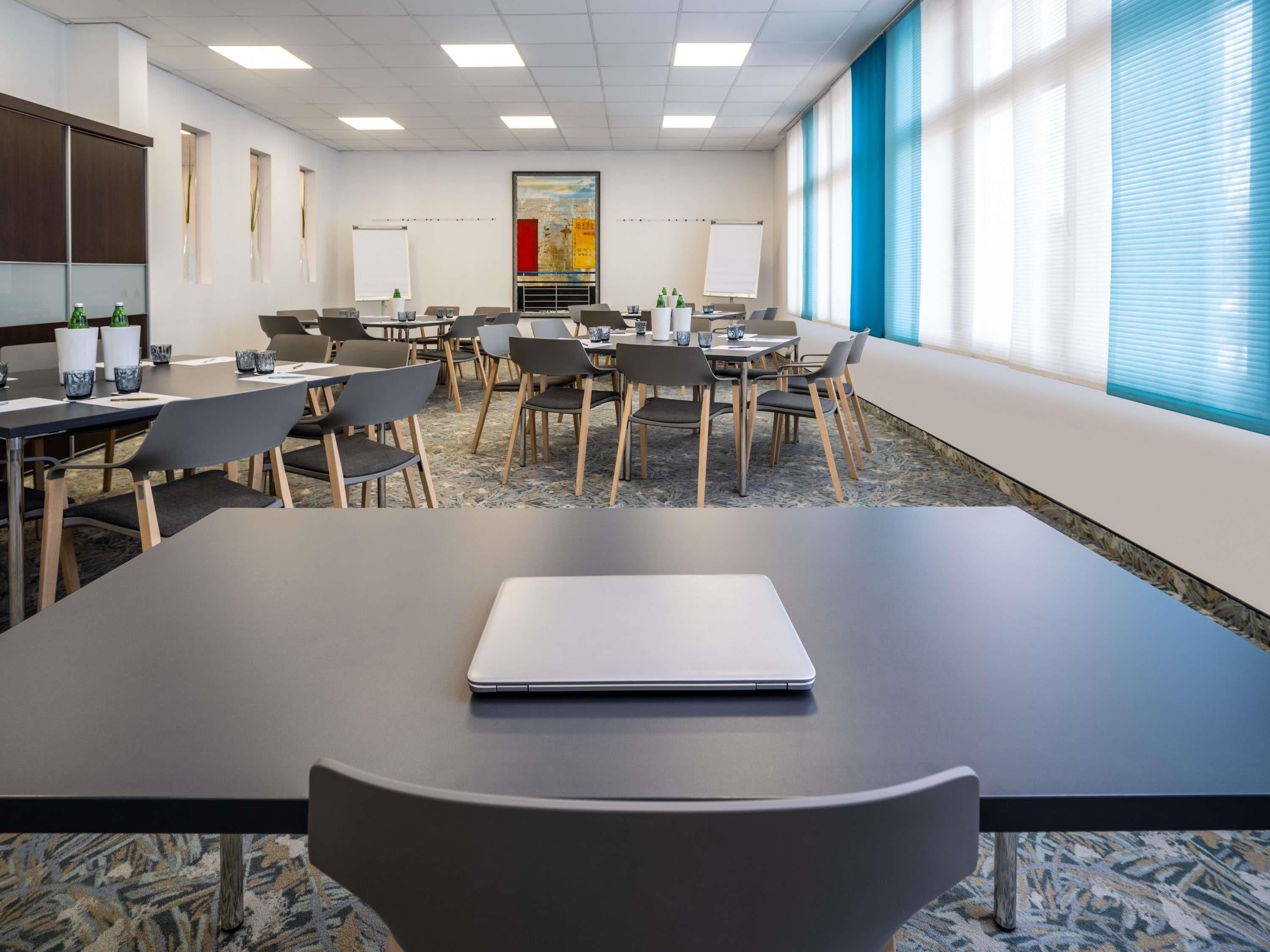 Una sala de conferencias con varias mesas, sillas y un ordenador portátil sobre una de ellas.
