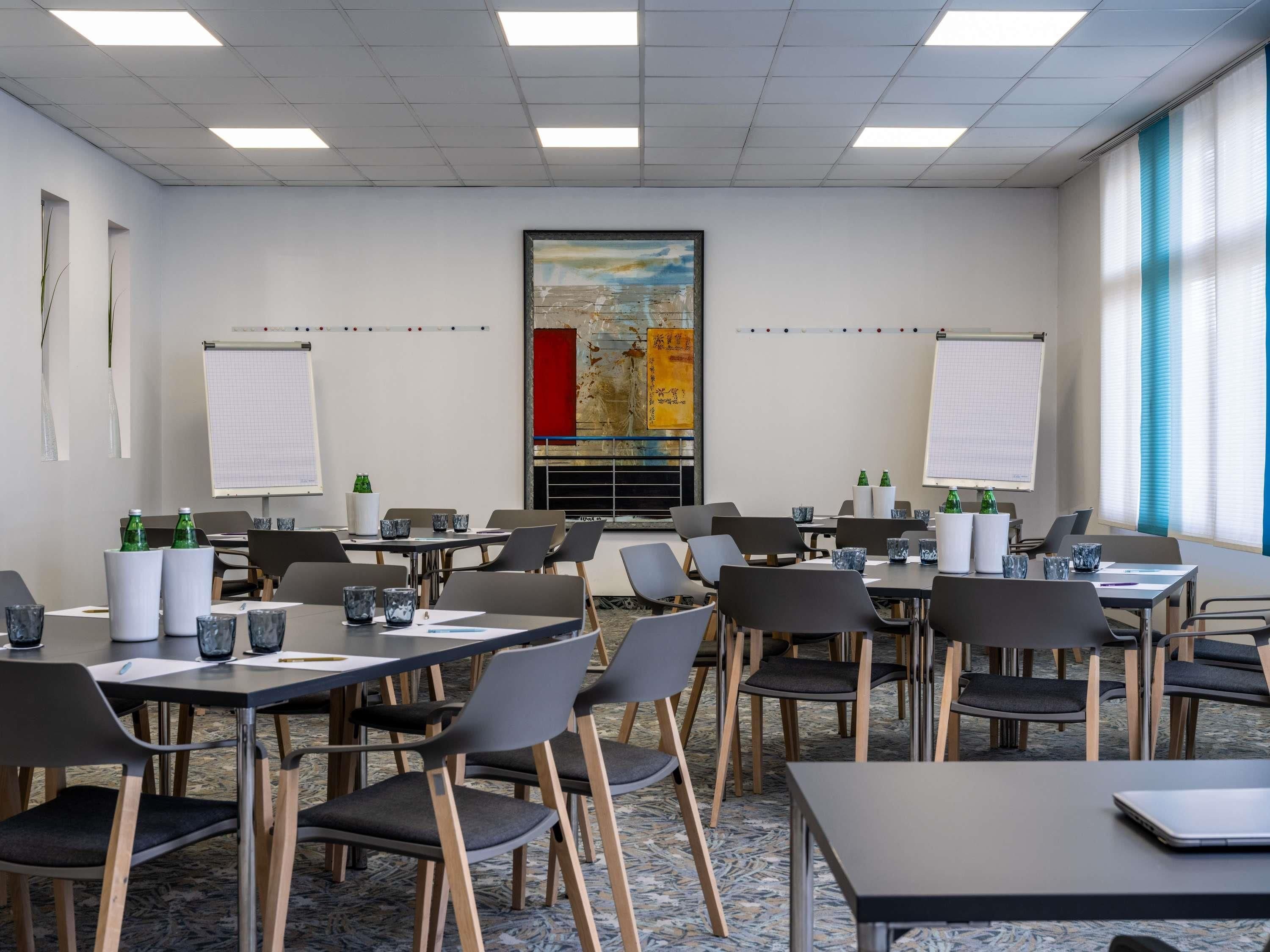 A conference room with tables, chairs, whiteboards, and a large painting on the wall.