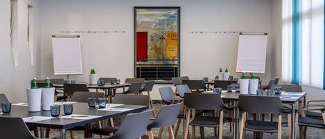 Uma sala de conferências com mesas, cadeiras, quadros brancos e uma grande pintura na parede.