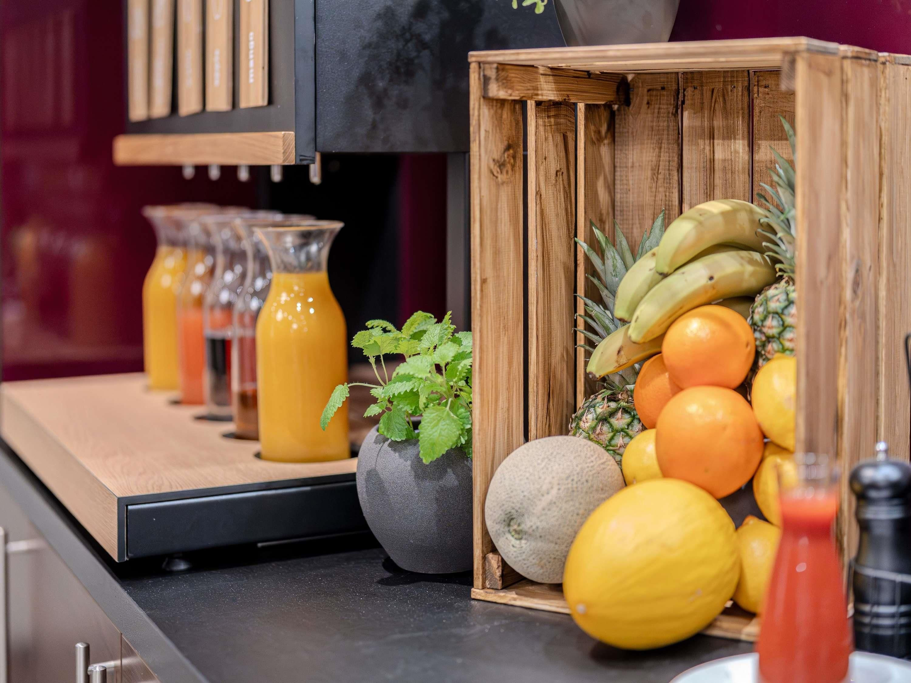 A kitchen counter with a wooden crate containing fruits, a potted plant, and a glass of orange juice.