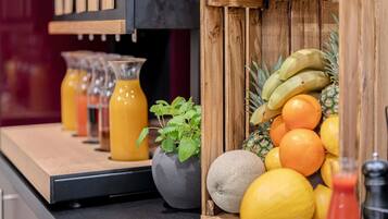 Una encimera de cocina con una cesta de madera que contiene frutas, una planta en maceta y un vaso de zumo de naranja.