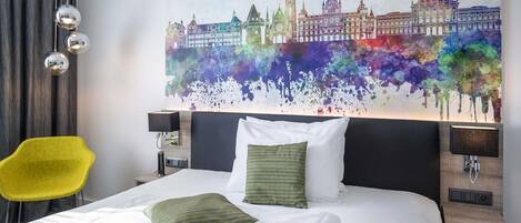 A hotel room with a bed, a yellow chair, a large cityscape painting, and two bedside lamps.