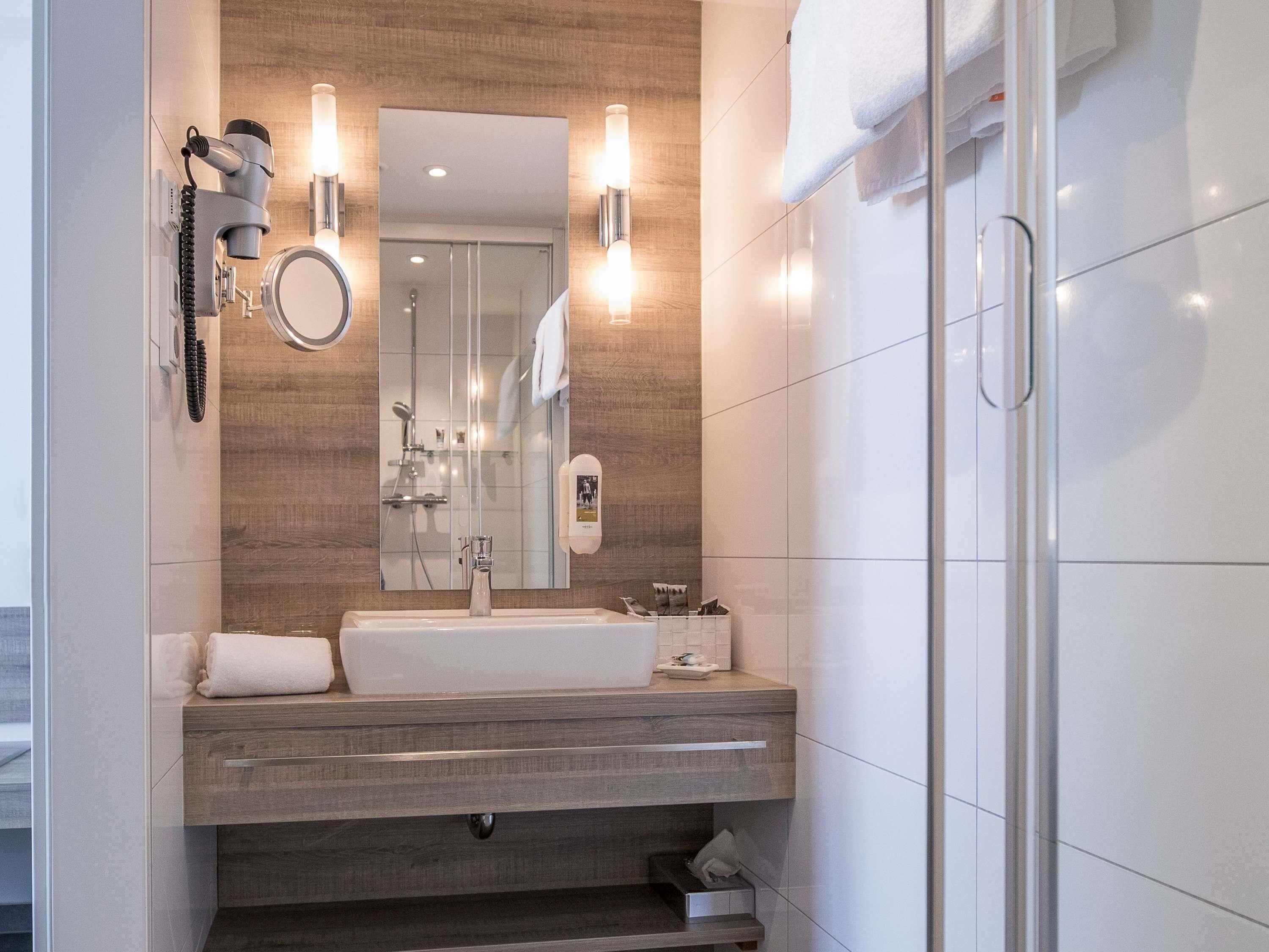 Une salle de bain moderne avec un grand miroir, un lavabo, un sèche-cheveux et un porte-serviettes.