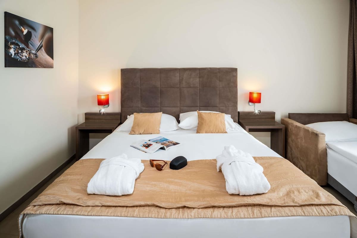 A hotel room with a large bed, two bedside tables, a nightstand, a magazine, and two towels.