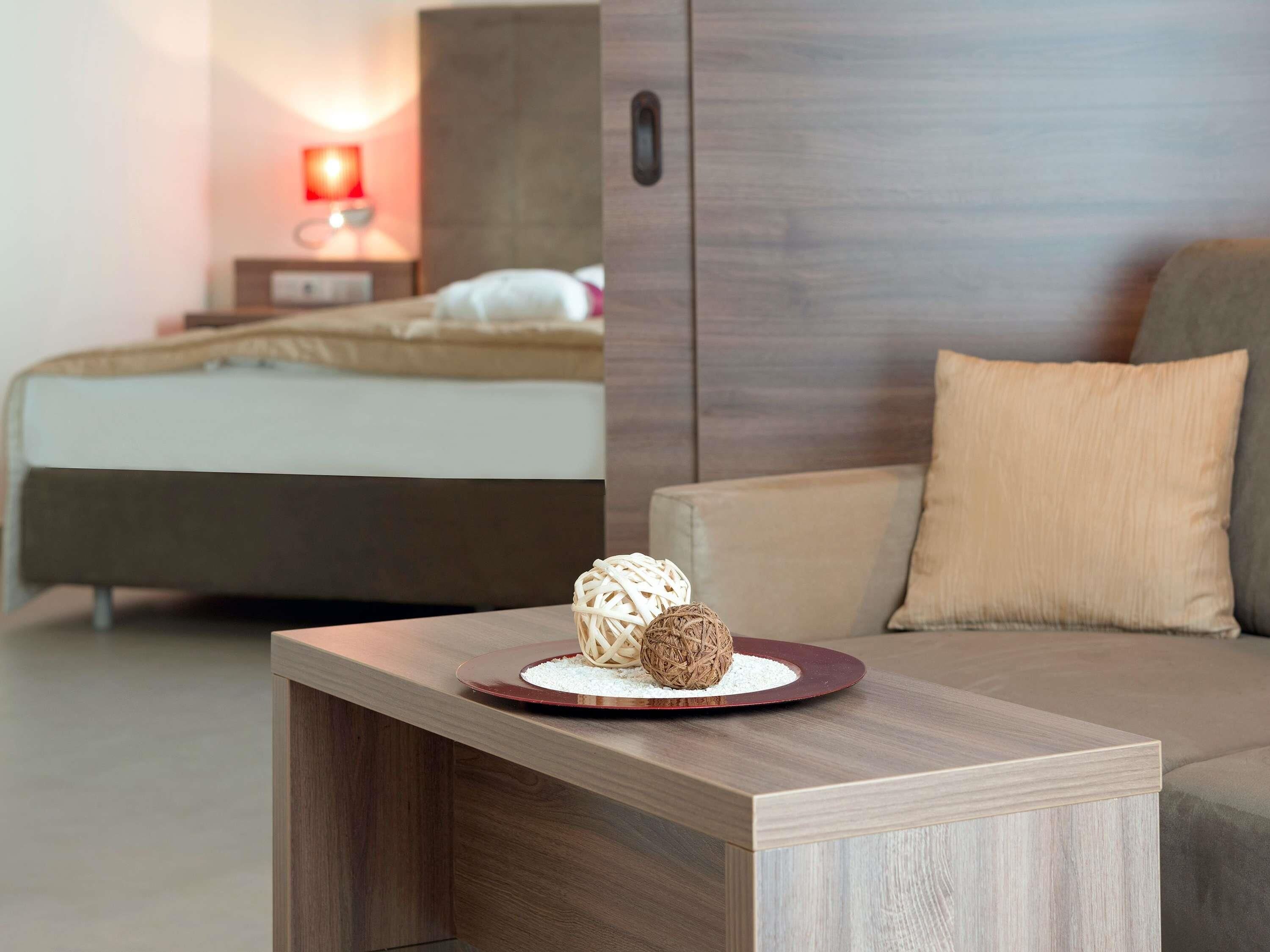 Une chambre d’hôtel moderne comprenant un lit, une table de chevet agrémentée d’objets décoratifs, un canapé et une table de nuit avec une lampe.