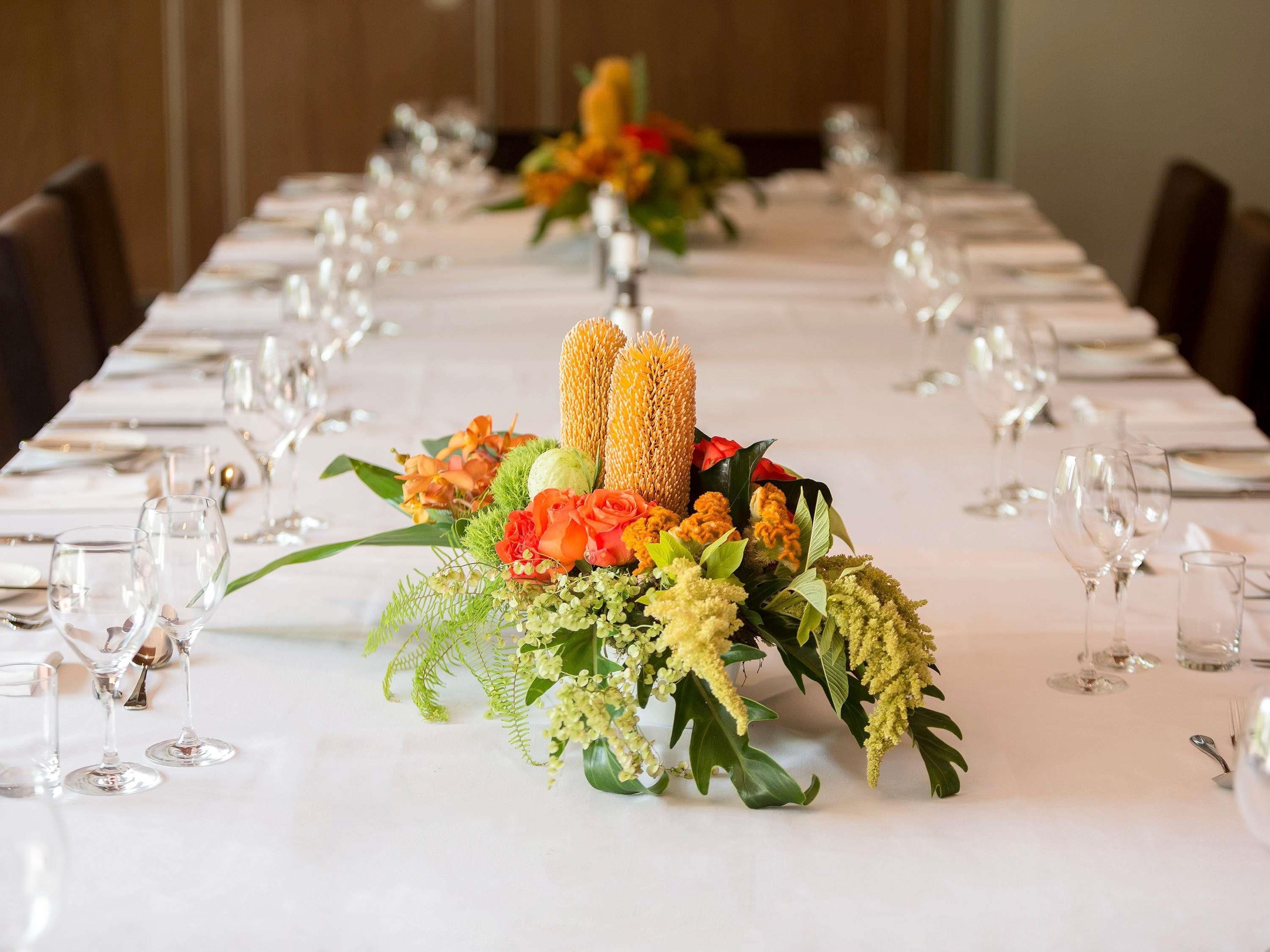 A long dining table with a floral centerpiece, arranged glasses, and a white tablecloth.