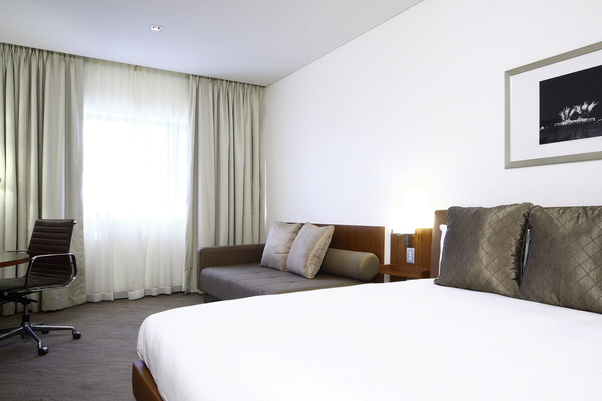 A hotel room with a bed, a sofa, a chair, and a framed picture on the wall.