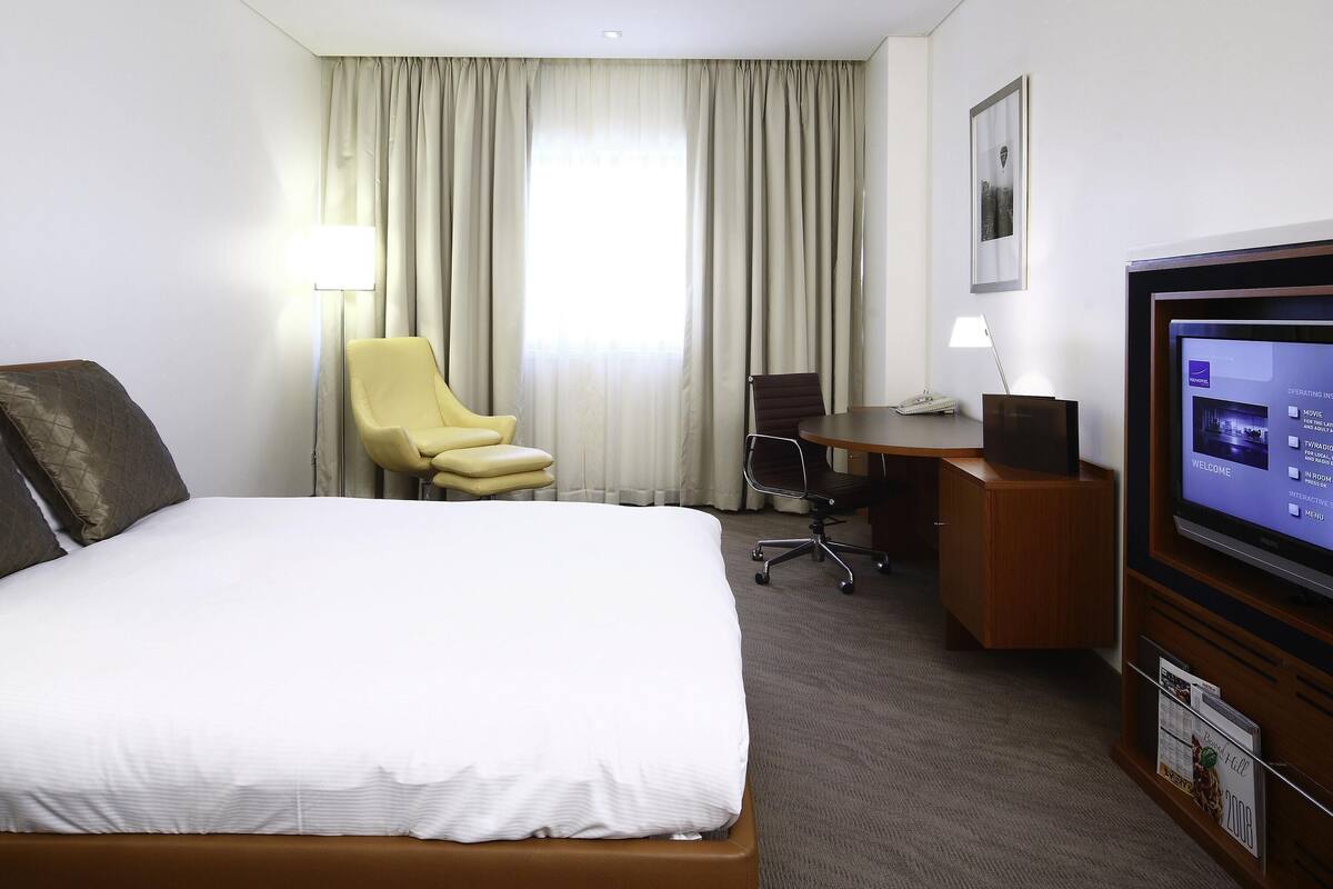 A hotel room with a bed, a desk, a chair, a television, and curtains.