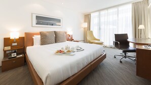 A hotel room with a large bed, bedside tables with lamps, a desk with a chair, and a window with curtains. - Novotel Canberra (Canberra)