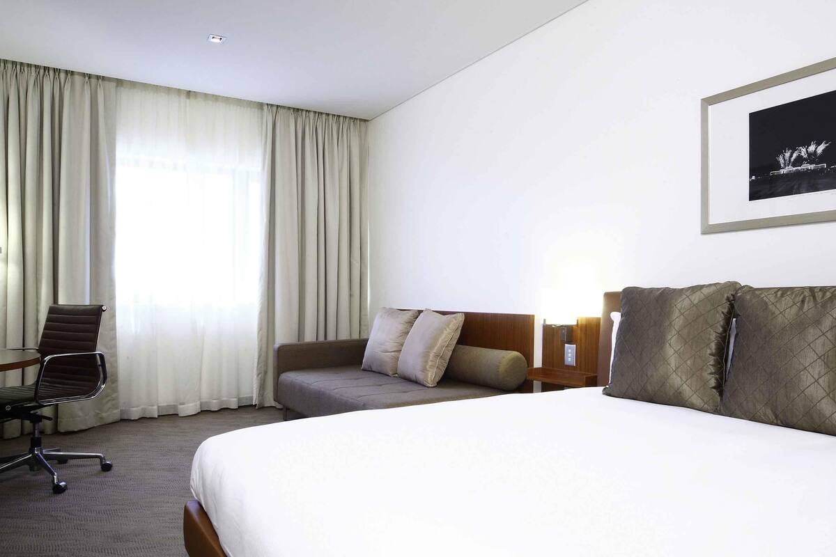 A hotel room with a bed, a sofa, a chair, and a framed picture on the wall.
