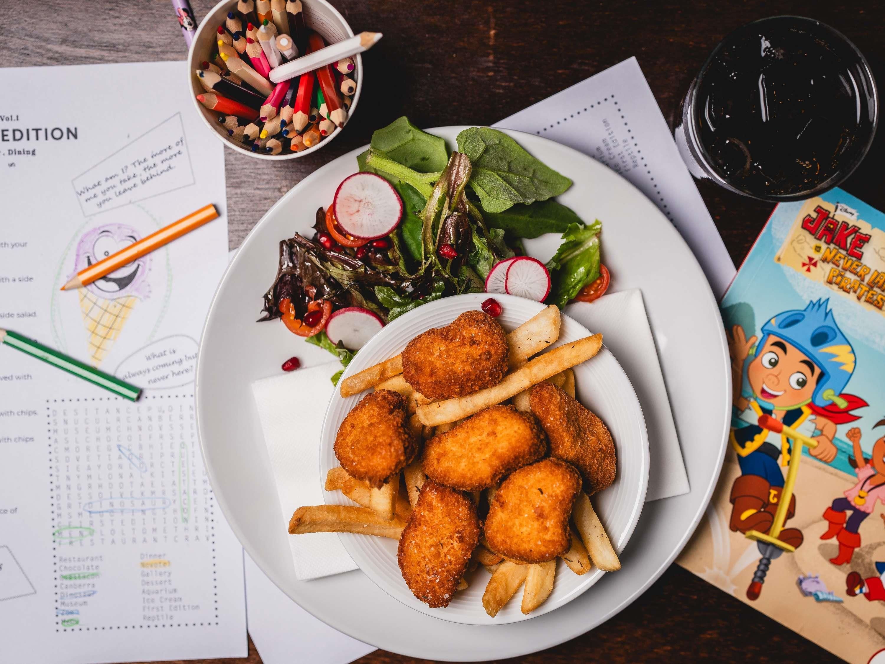 Une assiette de nourriture avec des frites et une salade, un pot rempli de crayons et un menu.