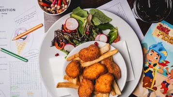 Une assiette de nourriture avec des frites et une salade, un pot rempli de crayons et un menu.
