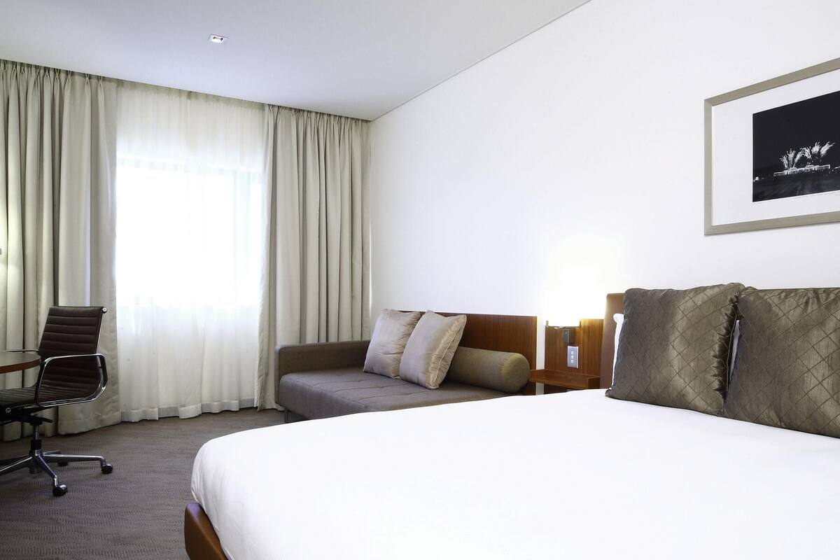 A hotel room with a bed, a sofa, a chair, and a framed picture on the wall.