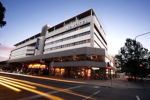 A modern hotel with a prominent 'NOVOTEL' sign, multiple floors, and a ground-level restaurant.