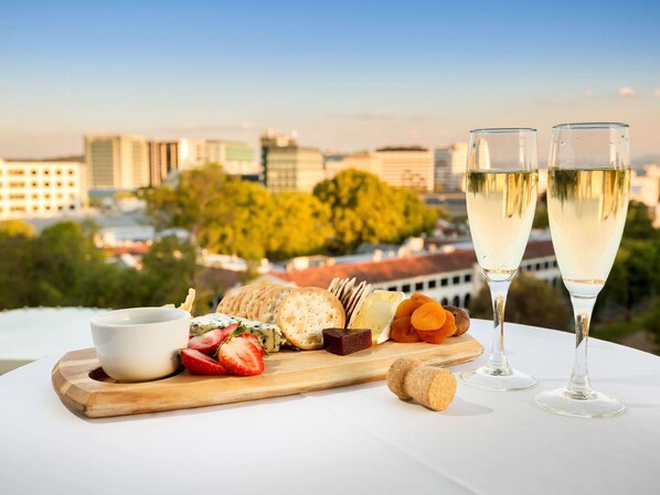 A table with a cheese board, two glasses of white wine, and a cityscape view.