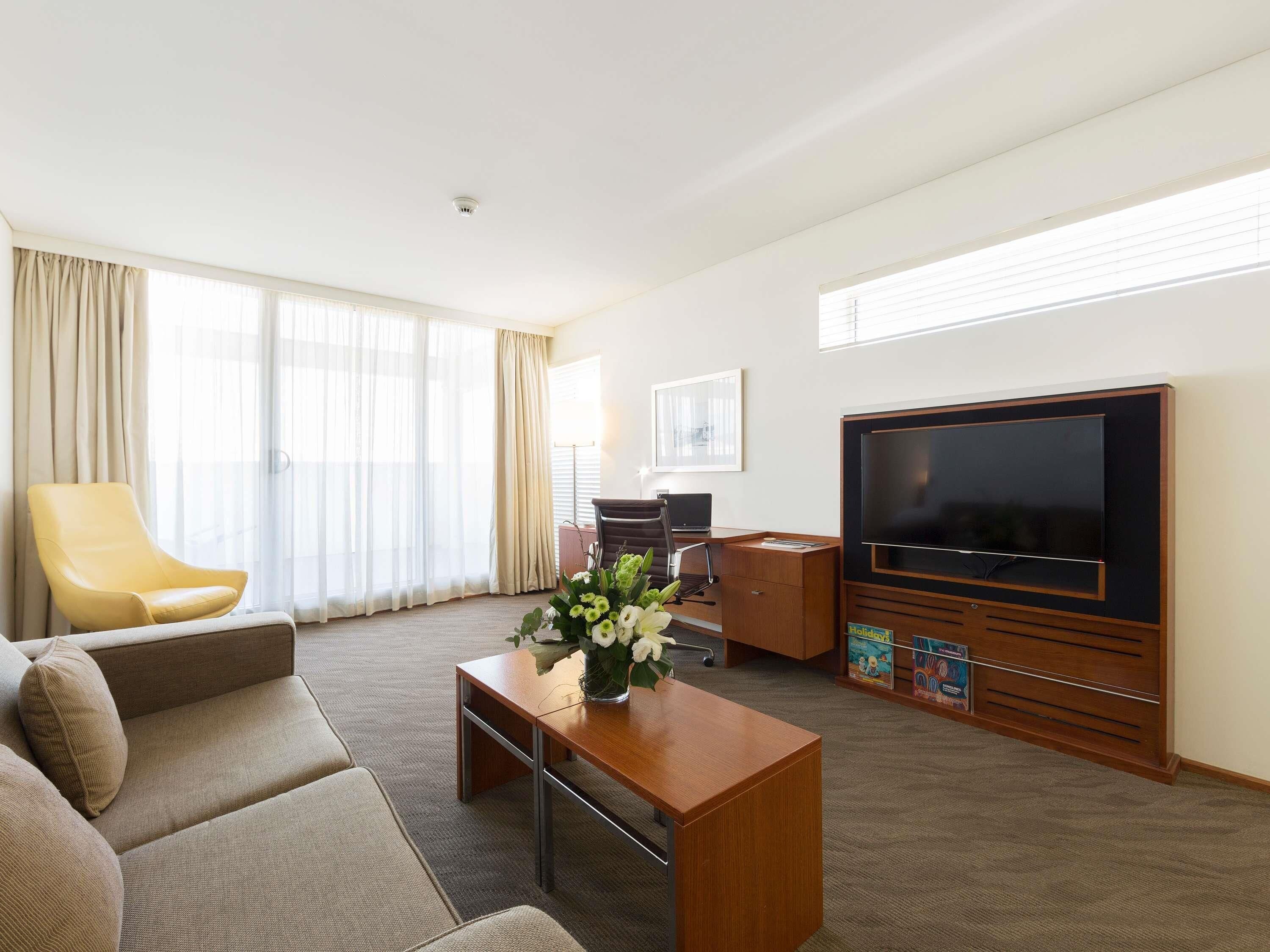 A hotel room with a sofa, a wooden desk, a television, and a large window with curtains.