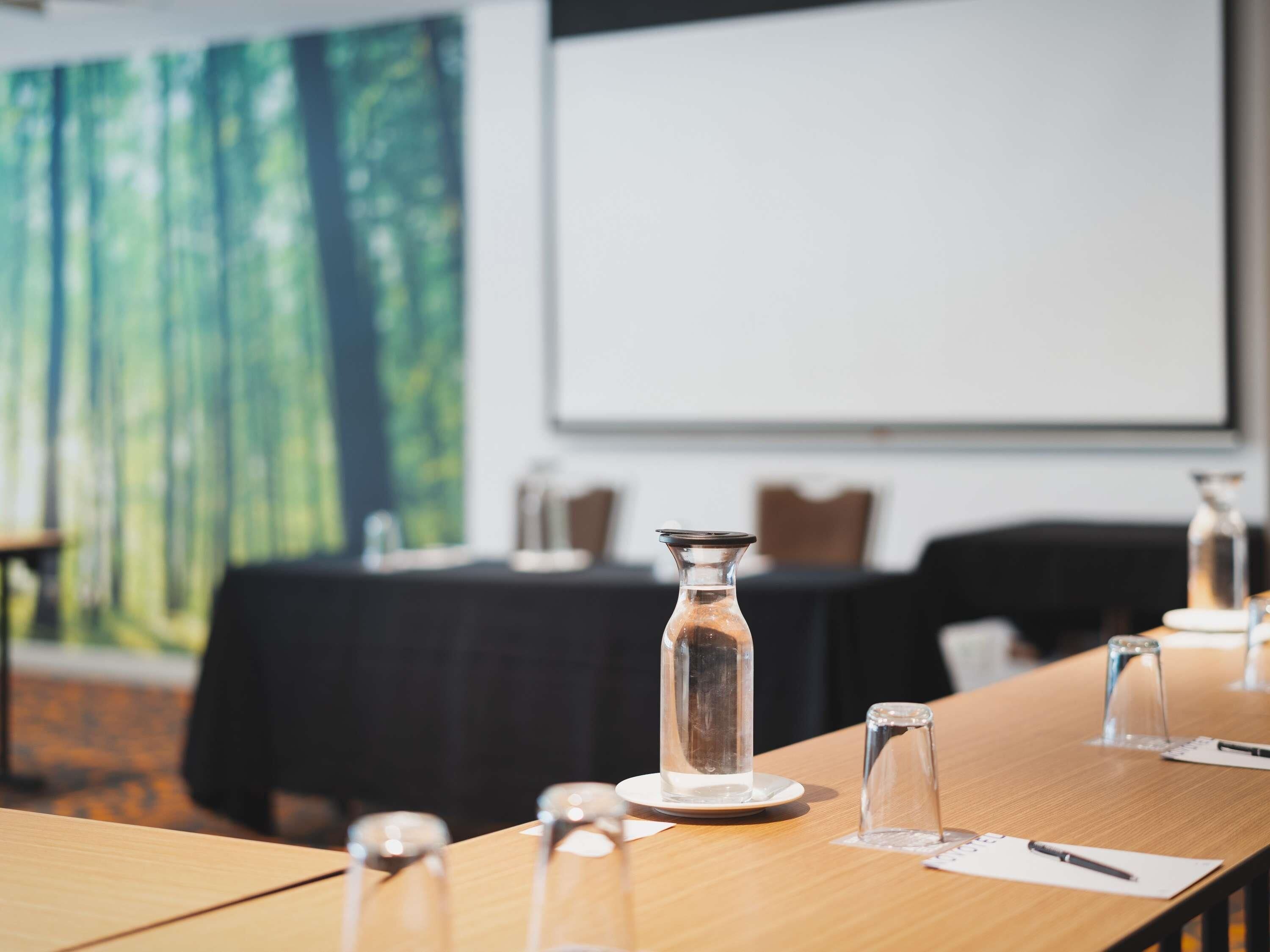 Een vergaderzaal met een lange tafel, helder glaswerk en een projectiescherm op de achtergrond.