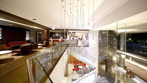 A modern hotel lobby with a glass railing, a staircase, and a seating area with red chairs. - Novotel Canberra (Canberra)