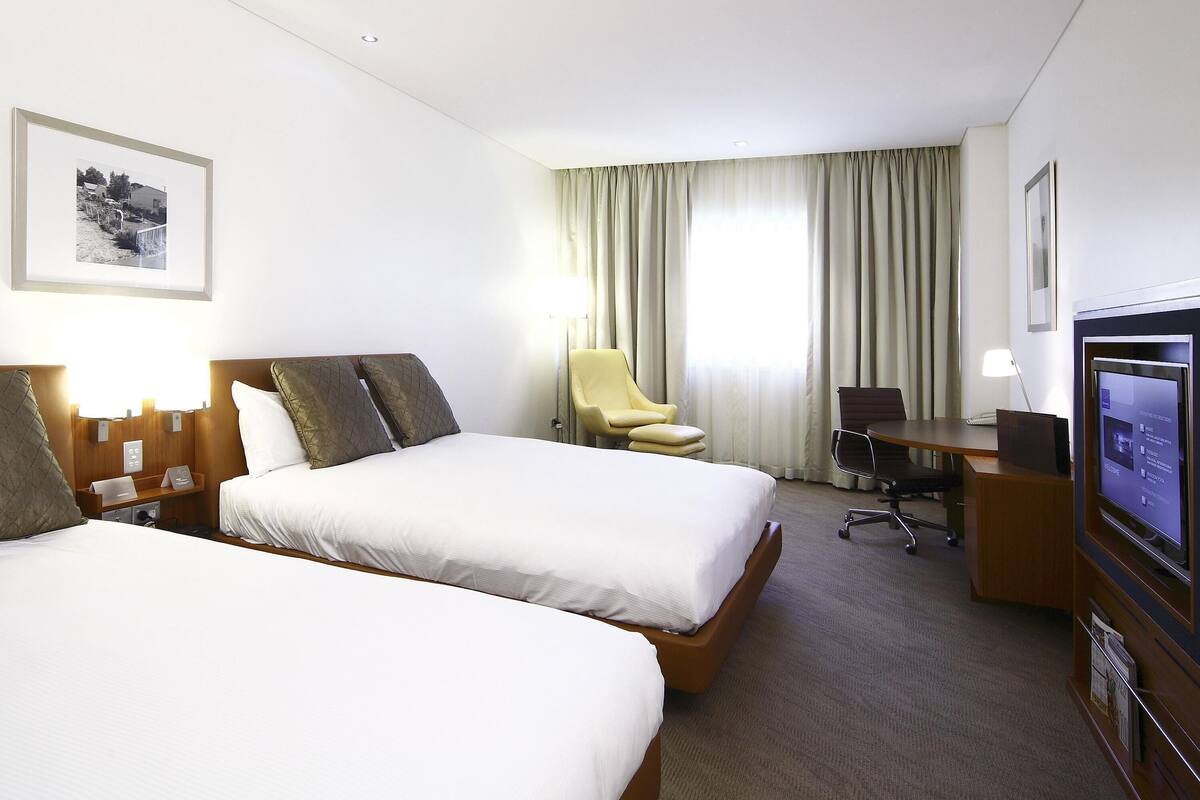 A hotel room with two beds, a desk, a chair, a television, and a window with curtains.