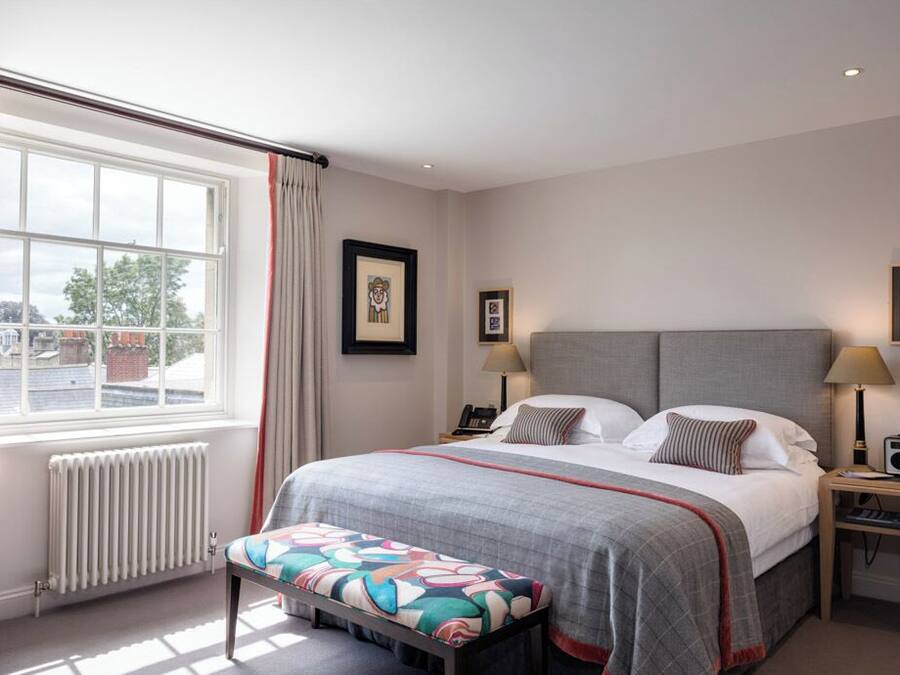 Un dormitorio ordenado con una cama grande, mesitas de noche, una ventana con cortinas y un radiador.