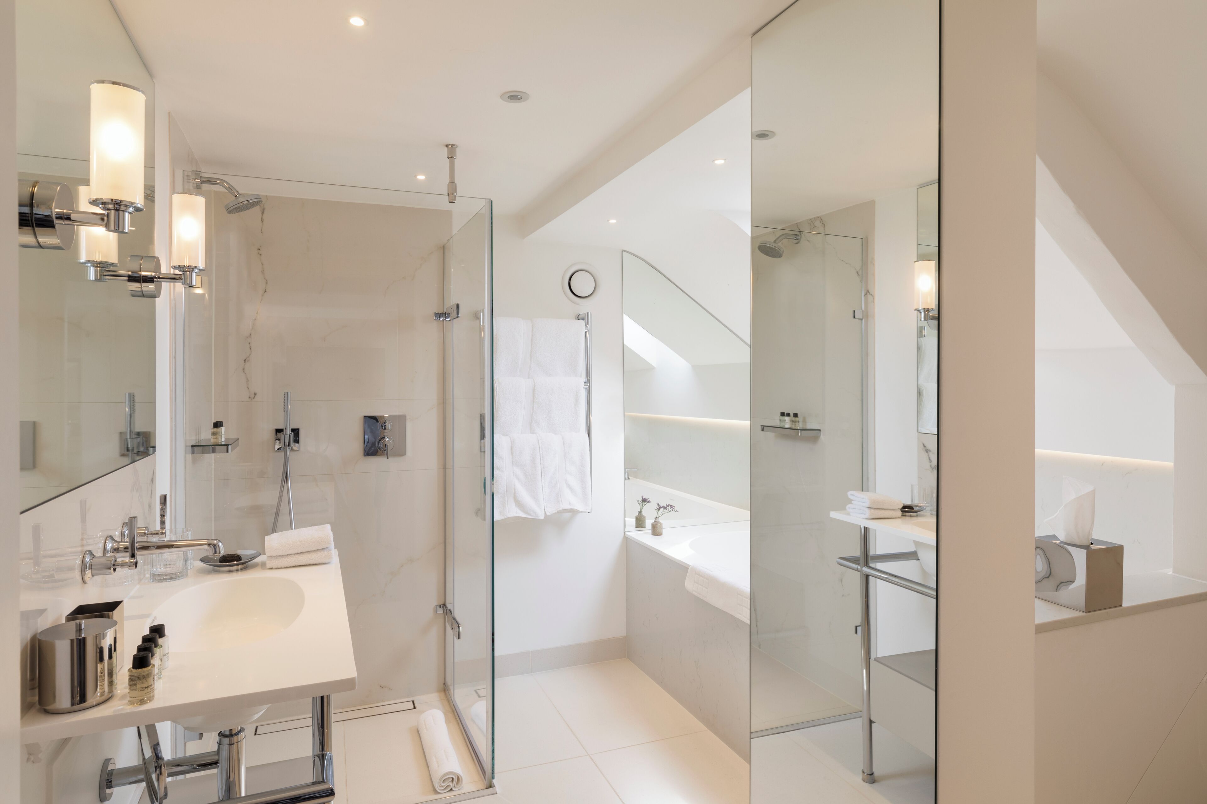 Un baño moderno con ducha de vidrio, lavamanos blanco y un espejo grande.