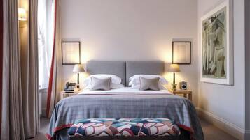 A hotel room with a large bed, two bedside lamps, a bedside telephone, a bench, and a painting on the wall.
