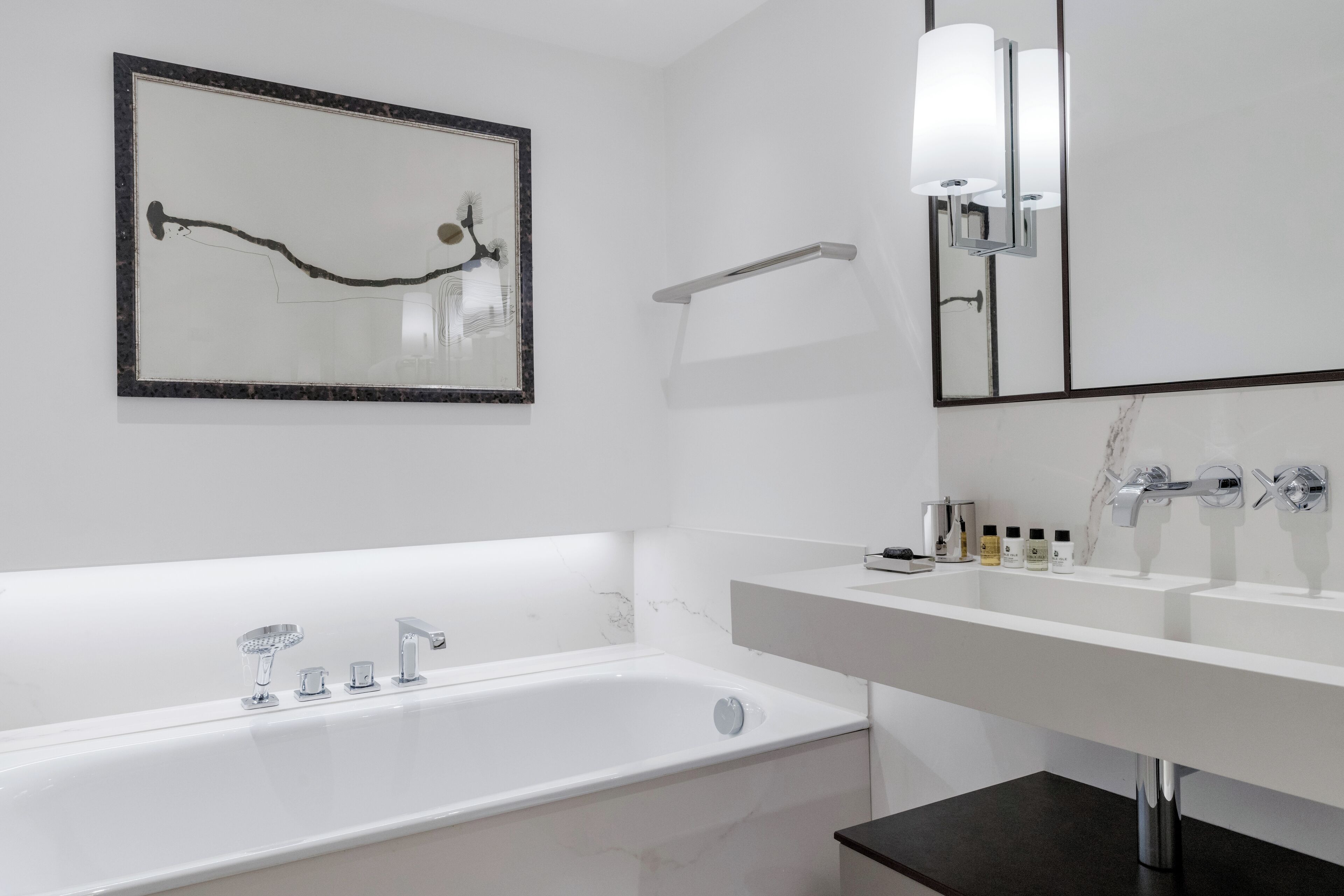 A modern bathroom with a large bathtub, a double sink, and a mirror with a light fixture.