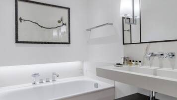 A modern bathroom with a large bathtub, a double sink, and a mirror with a light fixture.