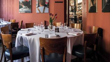 A dining area with round tables set for a meal, chairs, and a vase with flowers.