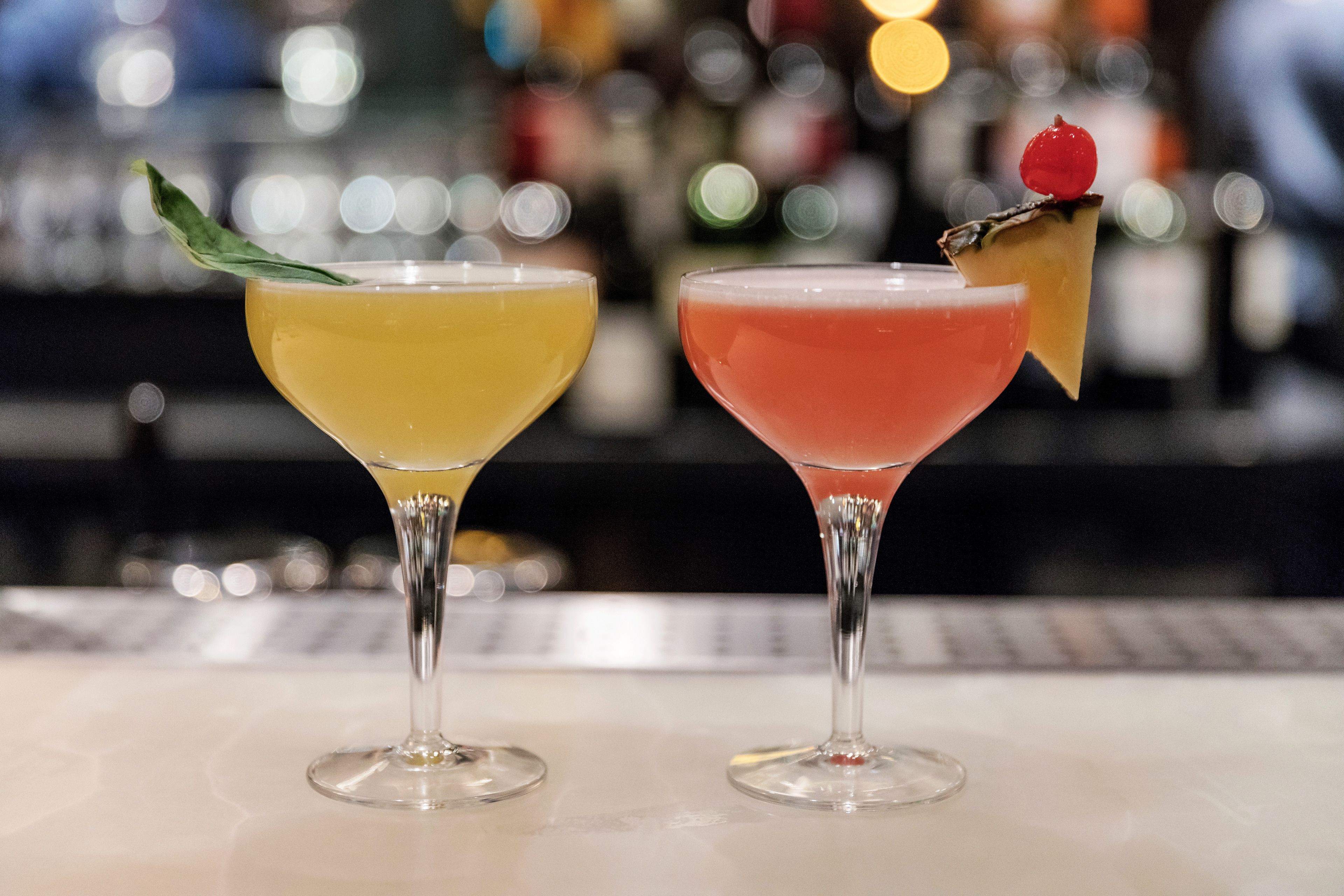 Due cocktail su un bancone del bar, con sullo sfondo sfocato una serie di bottiglie.
