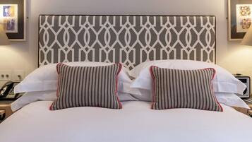 Una cama bien hecha con un cabecero estampado, dos almohadas con diseños a rayas y una franja roja decorativa.