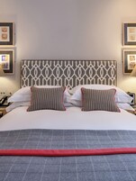 Una cama bien hecha con un cabecero estampado, dos almohadas con diseños a rayas y una franja roja decorativa.