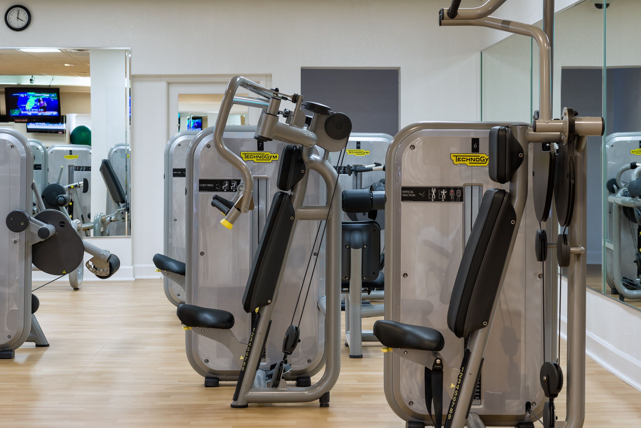 Un gimnasio con diversas máquinas de ejercicio, incluyendo una prensa de banca y una máquina de tracción vertical.