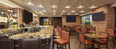 A bar area with a long counter, multiple seating options, and a brick wall.