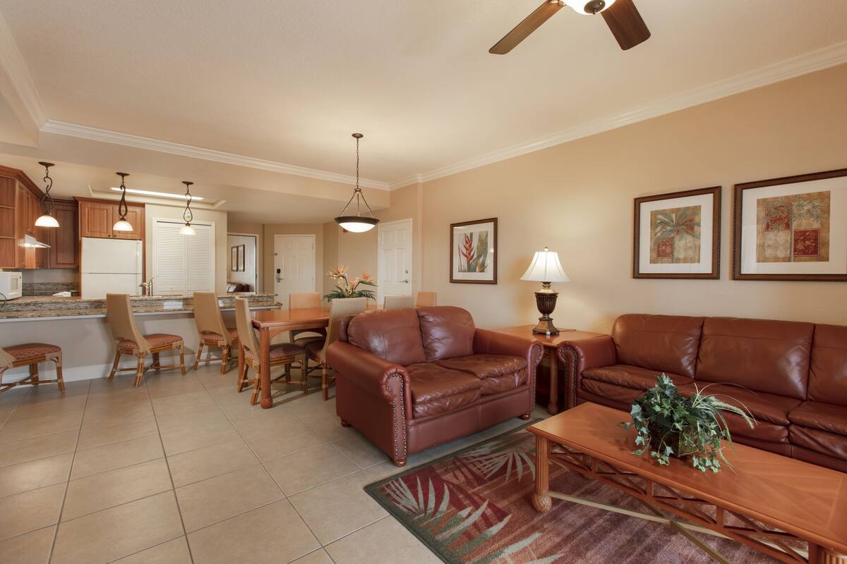 A spacious living room with a brown leather sofa, a wooden coffee table, and a dining area with chairs and a table.