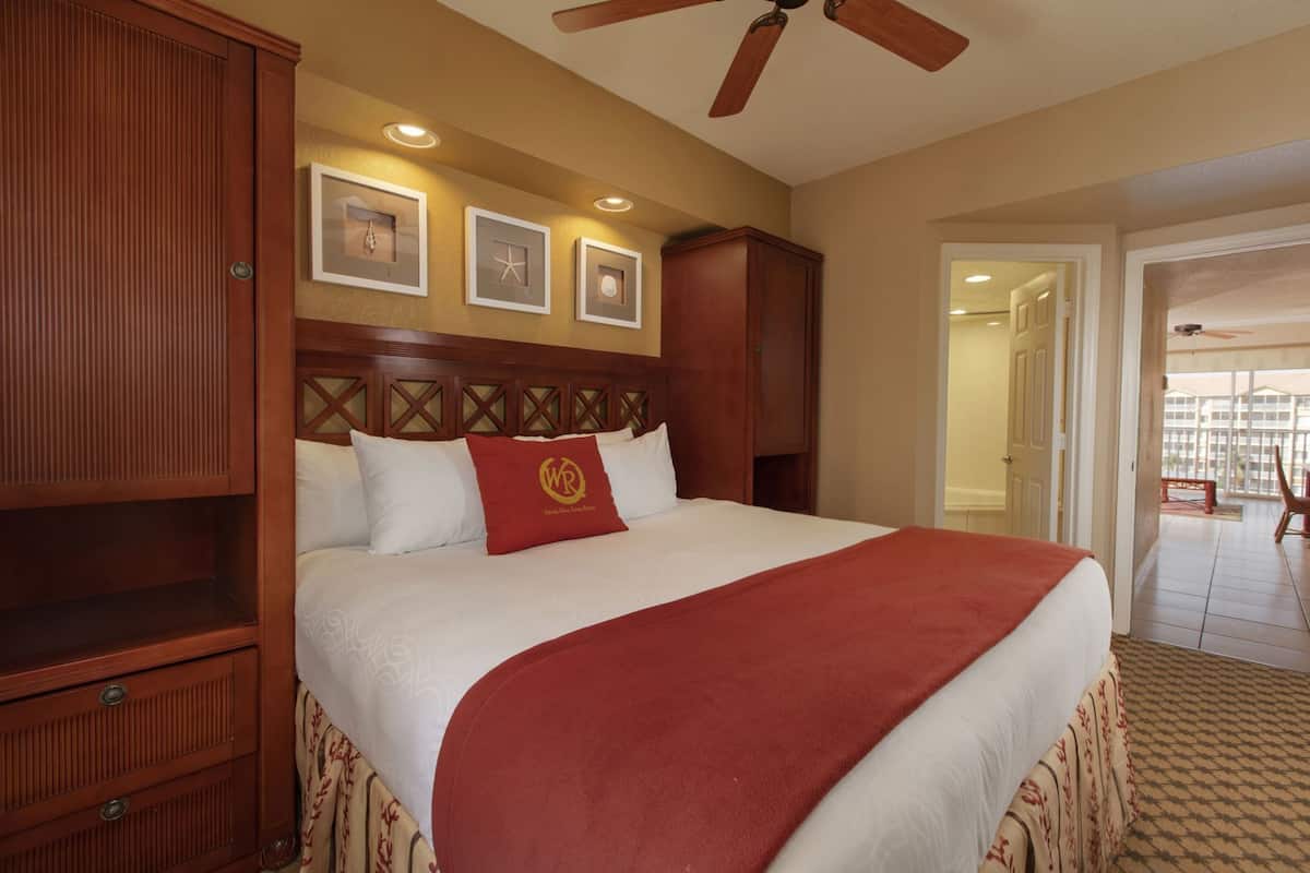 A hotel room with a large bed, wooden headboard, and a balcony with a view.