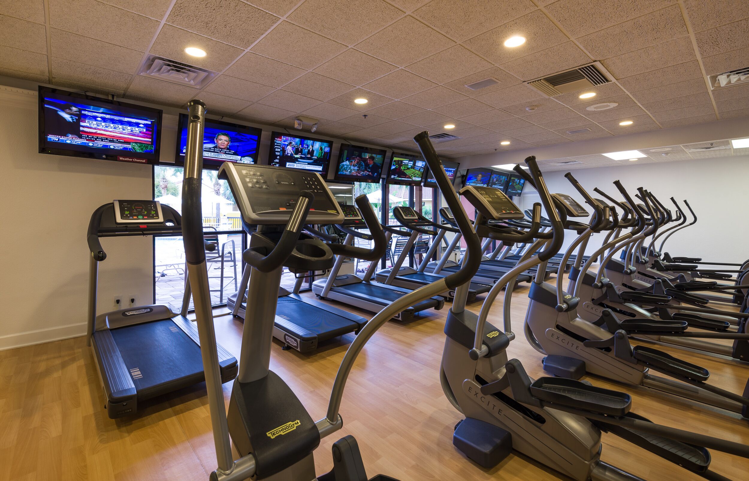 A gym with multiple treadmills and exercise bikes, equipped with digital screens displaying workout videos.