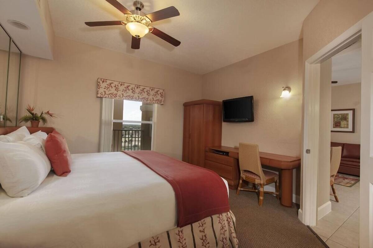 A hotel room with a bed, a desk, a chair, a television, and a ceiling fan.