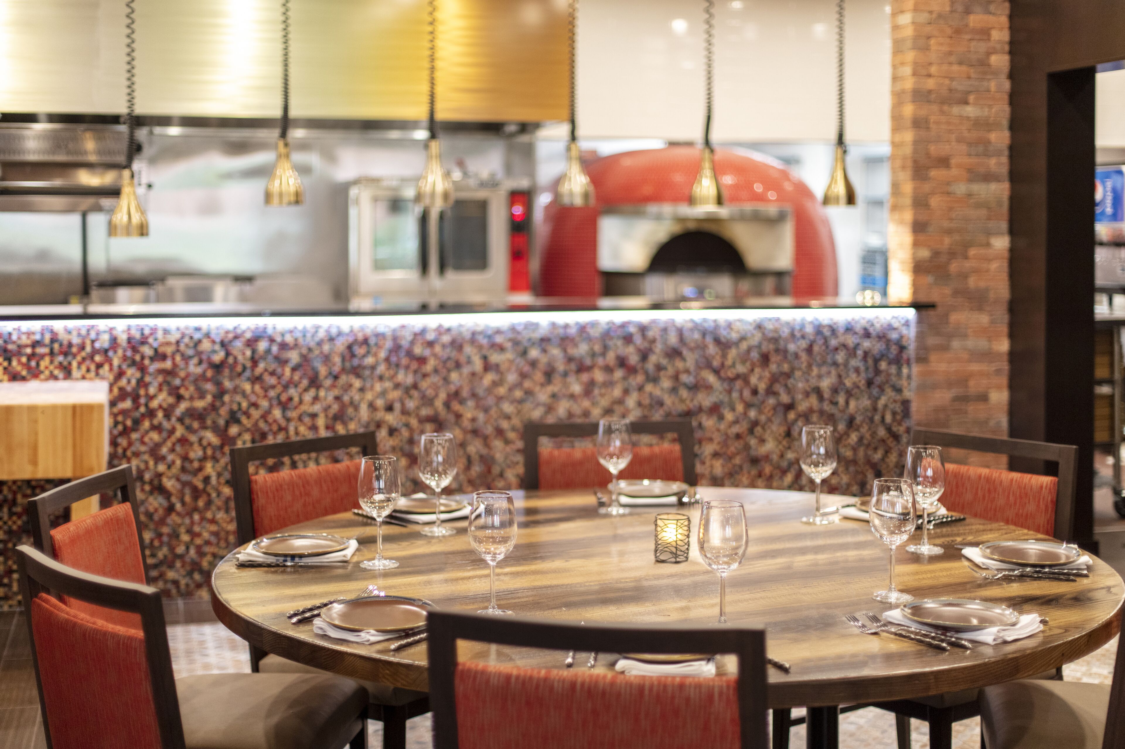 Un restaurante con una mesa redonda de madera dispuesta para comer, sillas tapizadas en rojo y lámparas colgantes.