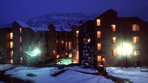 A multi-story hotel with illuminated windows and a snow-covered landscape in the background. - Carriage House Condominiums by All Seasons Resort (Park City)