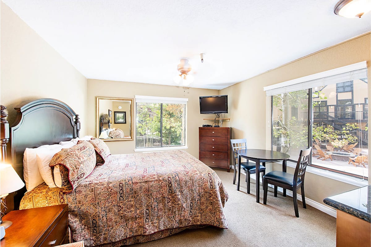 A bedroom with a bed, a desk, a chair, a television, and a window with a view of the outdoors.