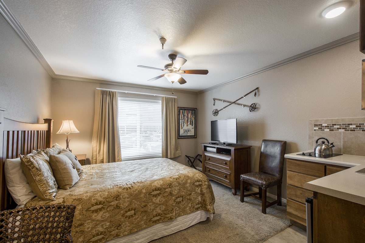 A hotel room with a bed, a desk, a chair, a television, and a ceiling fan.