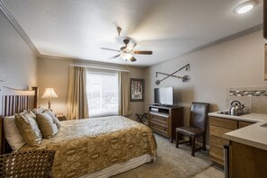 A hotel room with a bed, a desk, a chair, a television, and a ceiling fan.