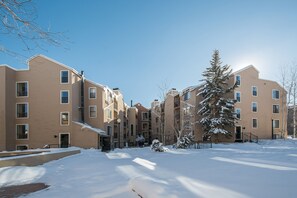 A multi-story residential building with a flat roof, multiple windows, and a snow-covered ground.