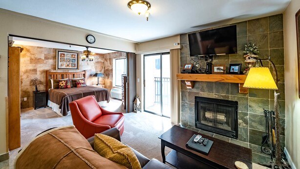 A modern living room with a fireplace, a red leather chair, a sofa, and a dining area with a table and chairs. - Carriage House Condominiums by All Seasons Resort (Park City)